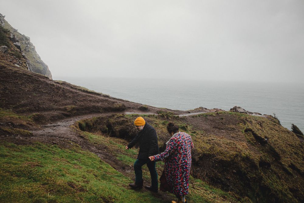 Two people walking along a misty coastal trail with dramatic ocean views.