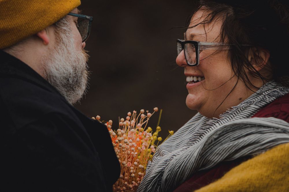 A couple shares a close moment with dried flowers between them on an overcast day.