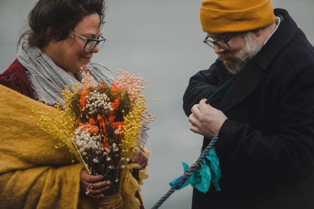 Two people examine a colorful bouquet of dried flowers and greenery.