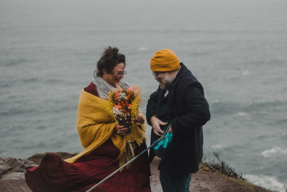 Two people sit together with flowers and crafting supplies on a coastal cliff.