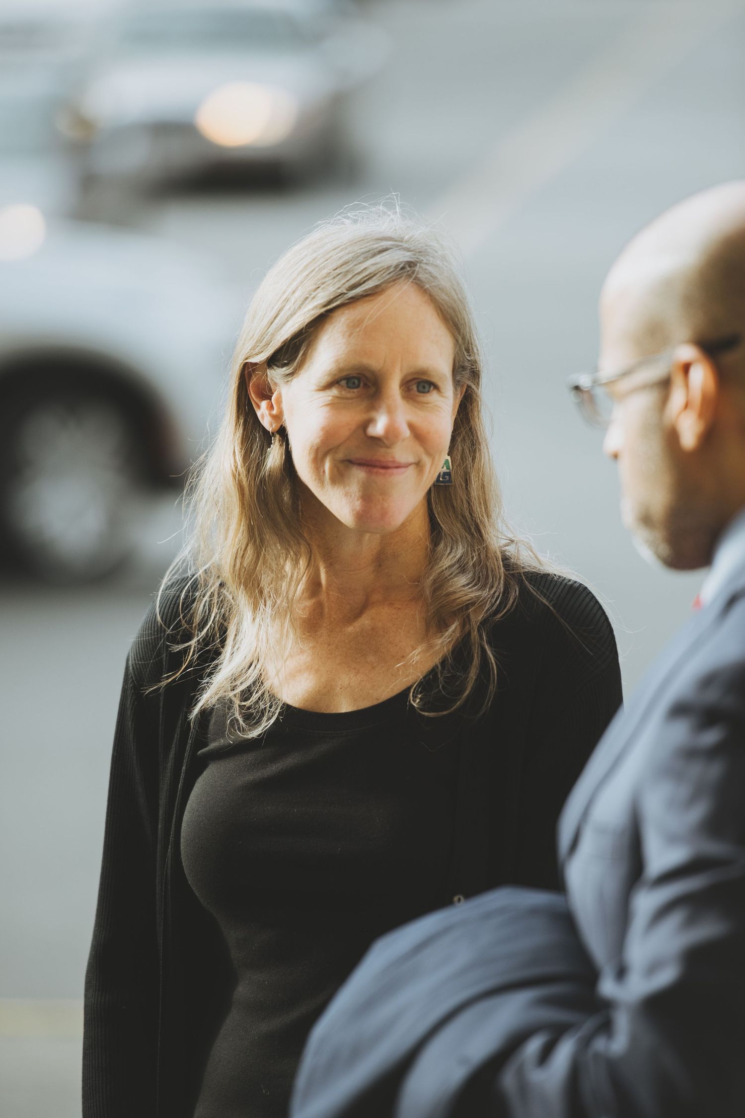 Two people having a conversation outdoors, one wearing a black top and the other in business attire.