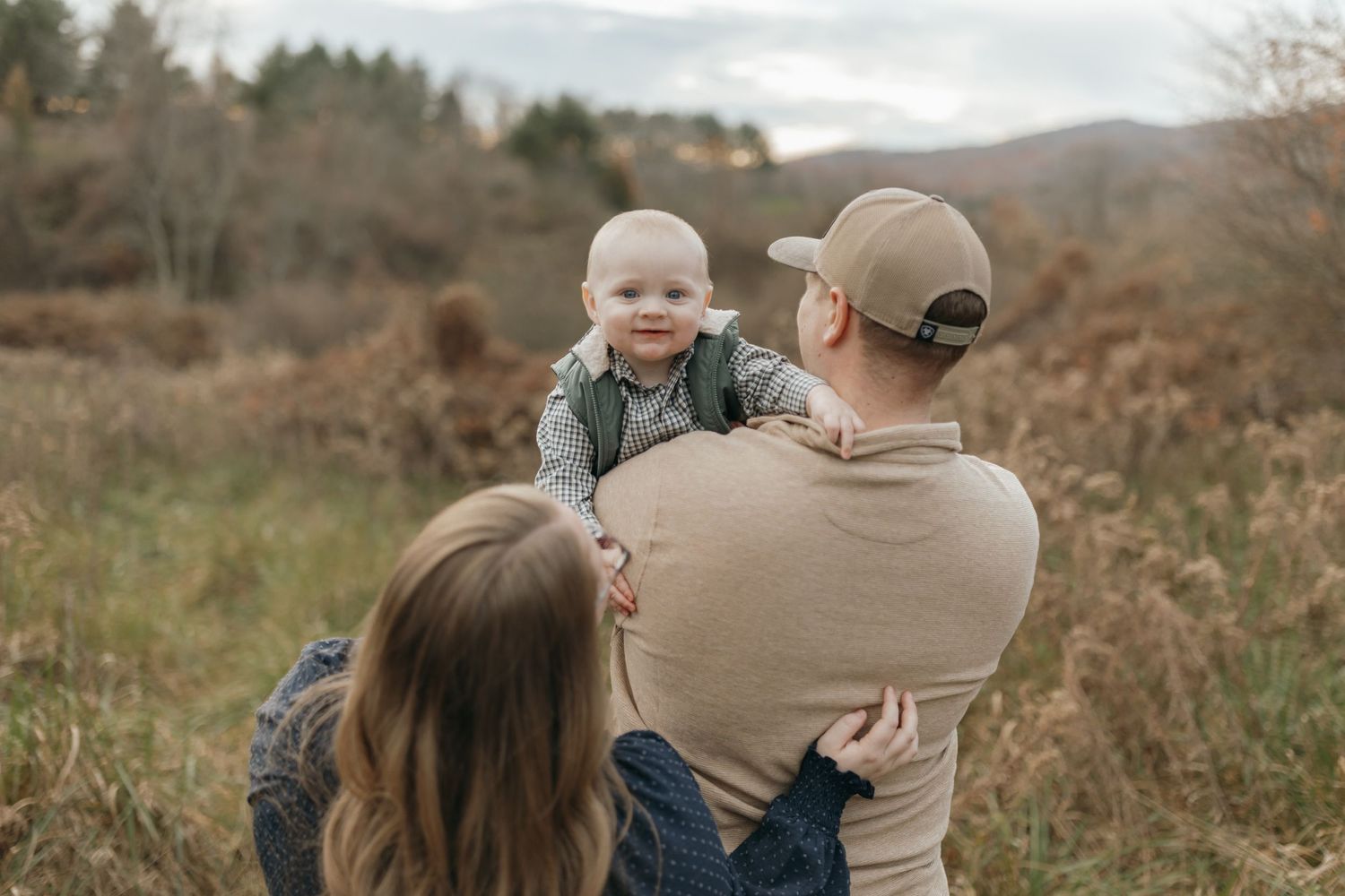Family sharing tender moment in field with mountains and forest in background during fall.