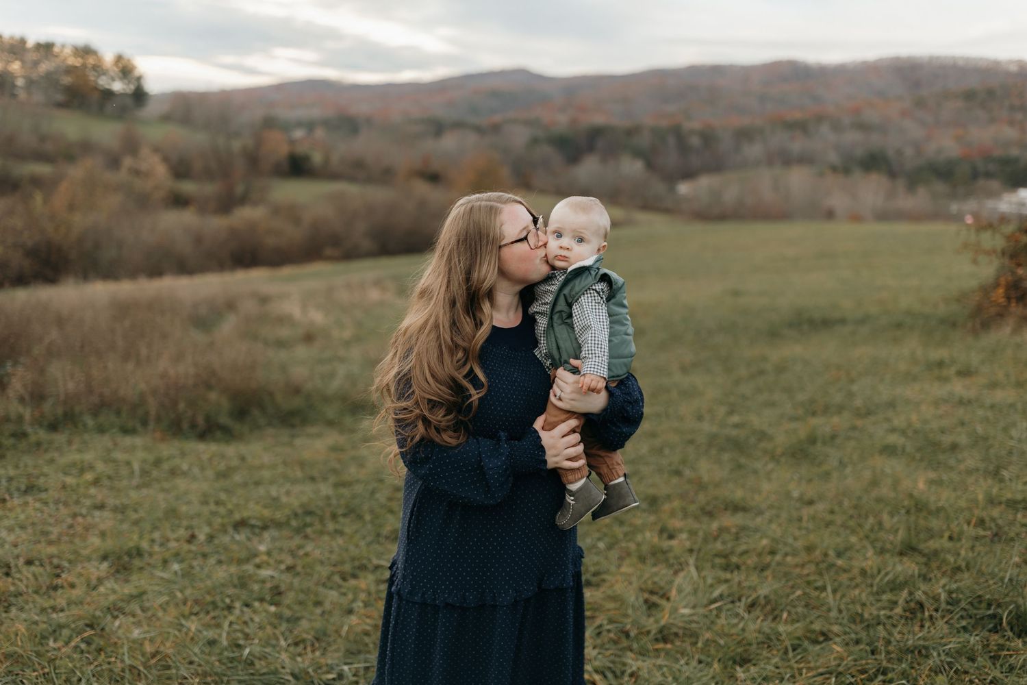 Mother and baby sharing a tender embrace in an autumn field with rolling hills in the background.