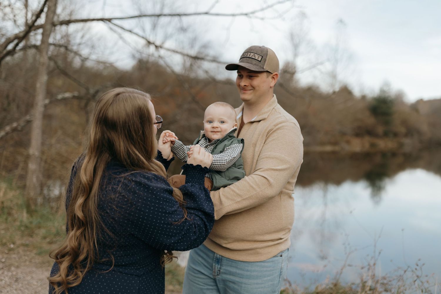Family gathering by a serene lake surrounded by autumn foliage and bare trees.