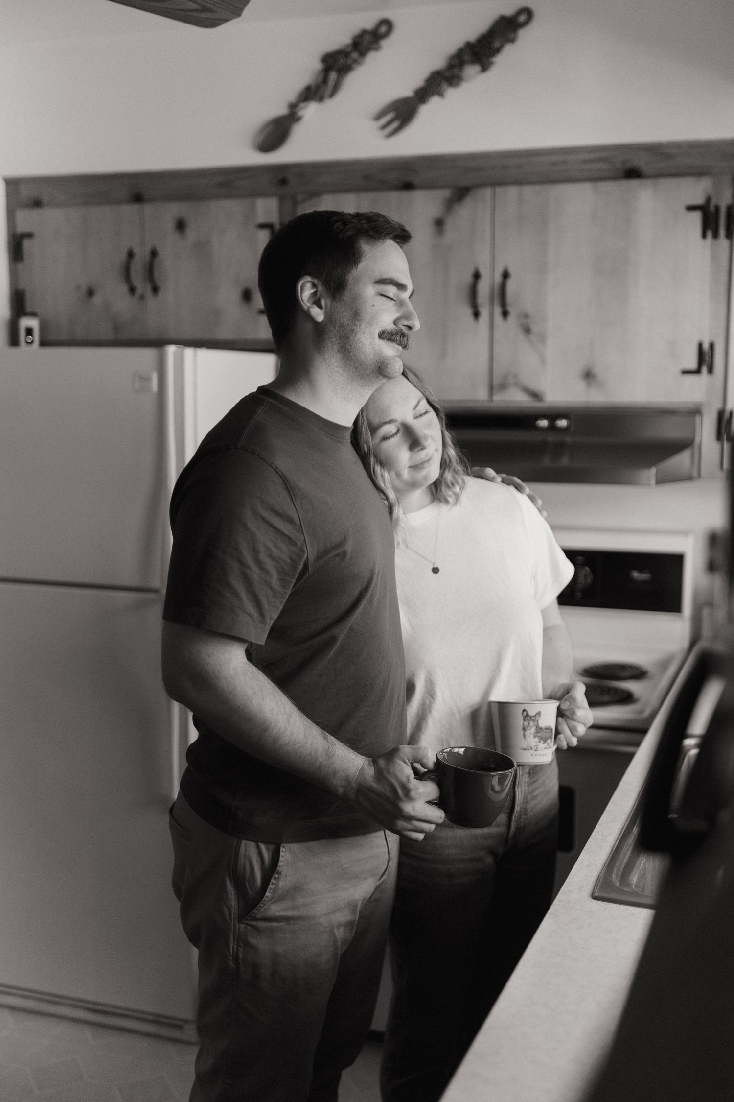 A black and white photo capturing a sweet moment between two people in their kitchen.