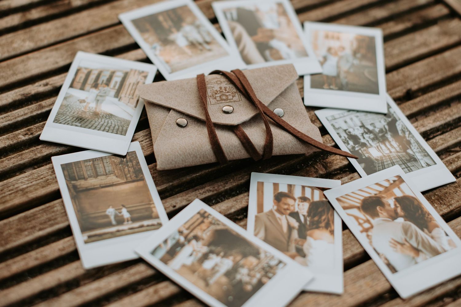 Vintage Polaroid photographs scattered around brown leather journal on wooden slat surface.
