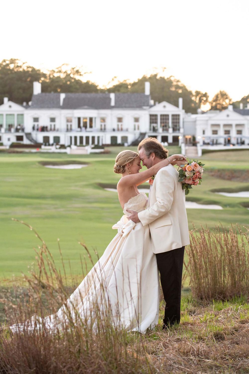 A romantic wedding moment overlooking a scenic golf course and white clubhouse during golden hour.