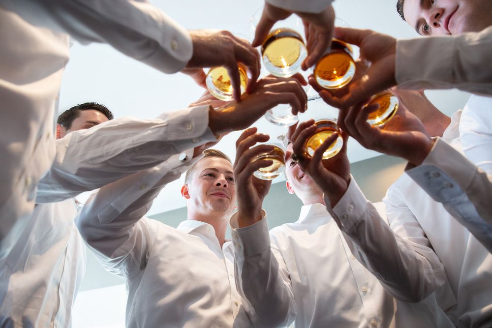 Group of people in white shirts toasting drinks together in a circle from below.