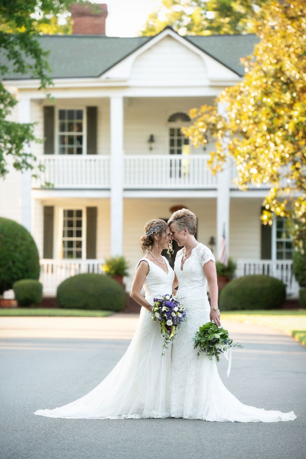 A beautiful outdoor wedding scene shows two brides in white dresses against a classic white colonial house.