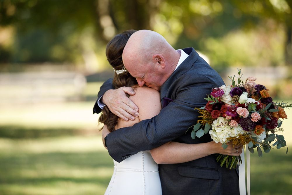 Romantic outdoor wedding scene with couple embracing while holding a vibrant fall bouquet in sunlit garden.