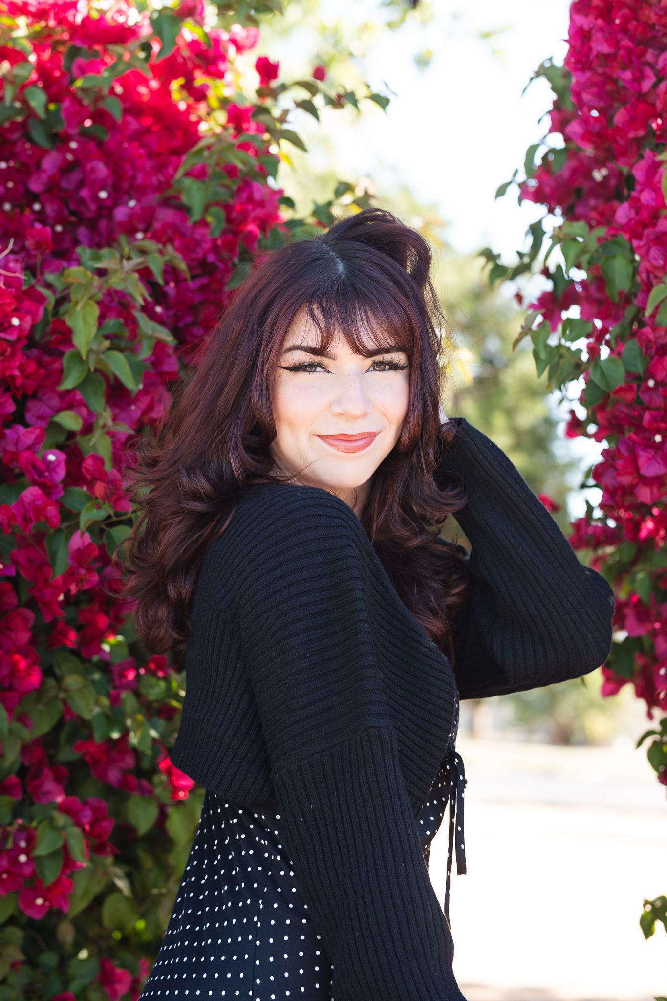 Stylish pose against blooming red bougainvillea in black sweater and polka dot dress.