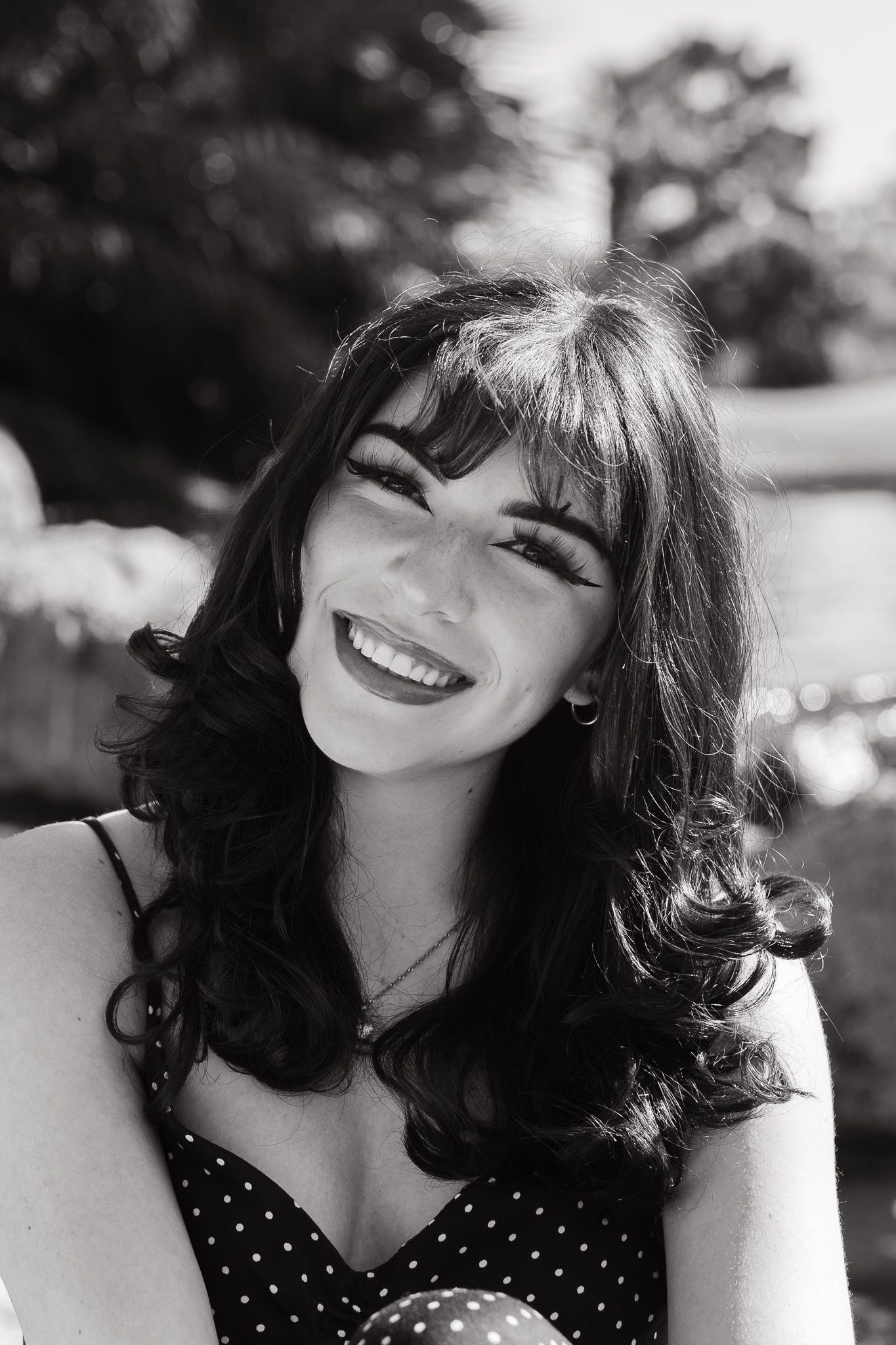 Black and white portrait showing a genuine smile and dark curly hair against a blurred background.