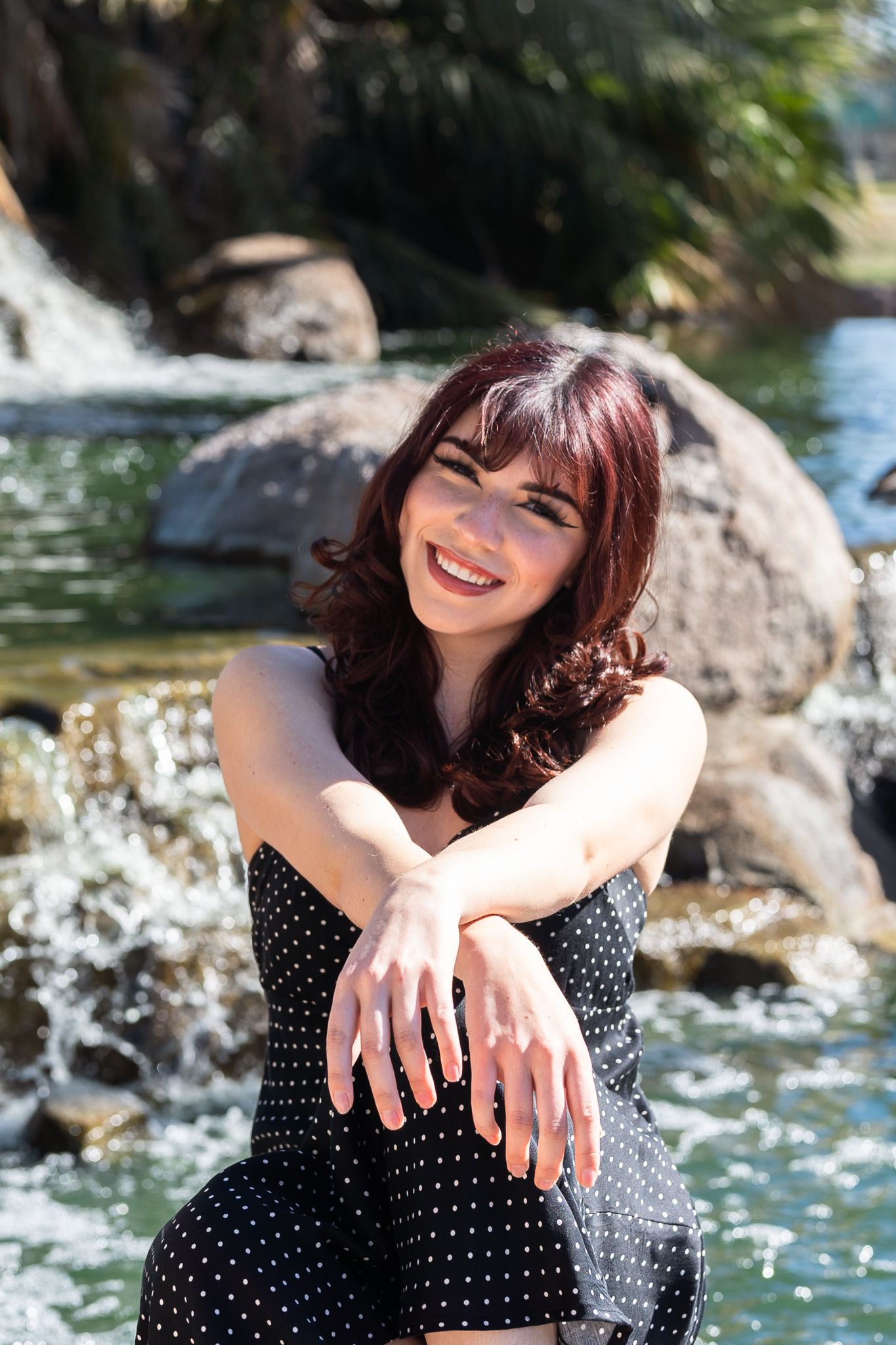 Candid outdoor photo by a water feature wearing a spotted dress on a bright day.