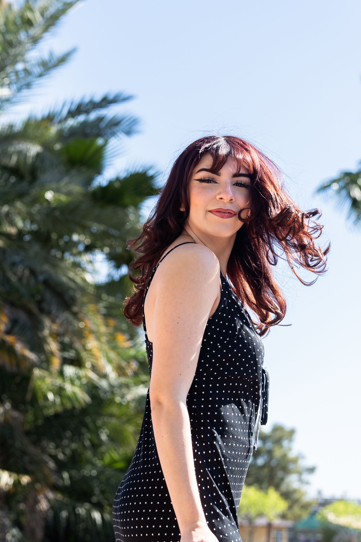Sun-drenched portrait with wind-swept hair against tropical palm trees and blue sky.