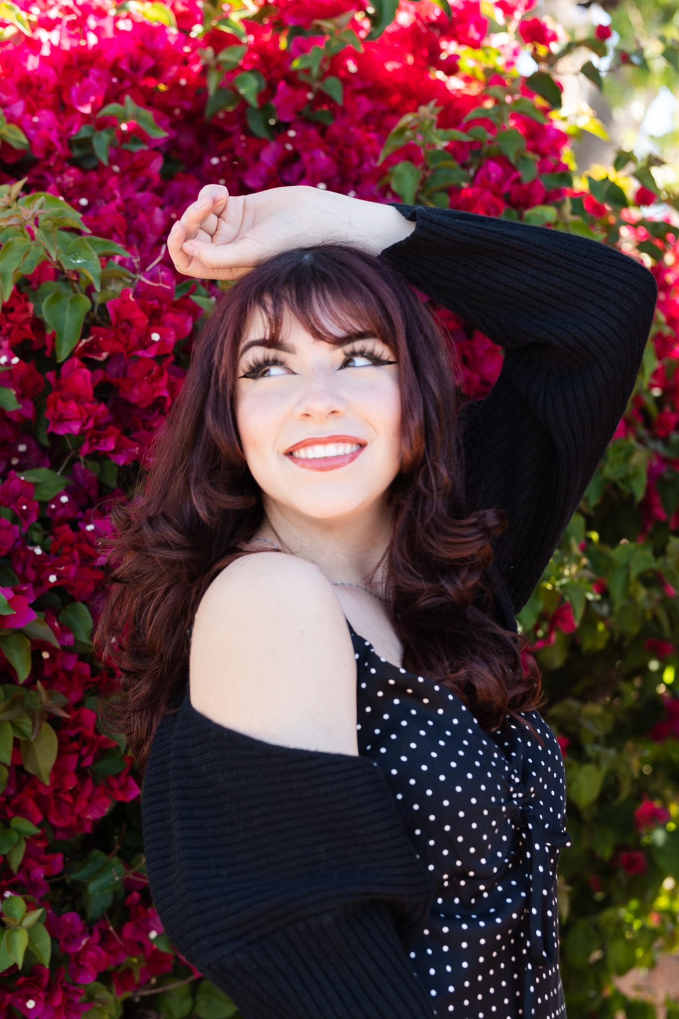 Portrait against vibrant bougainvillea flowers wearing black cardigan and polka dot dress.