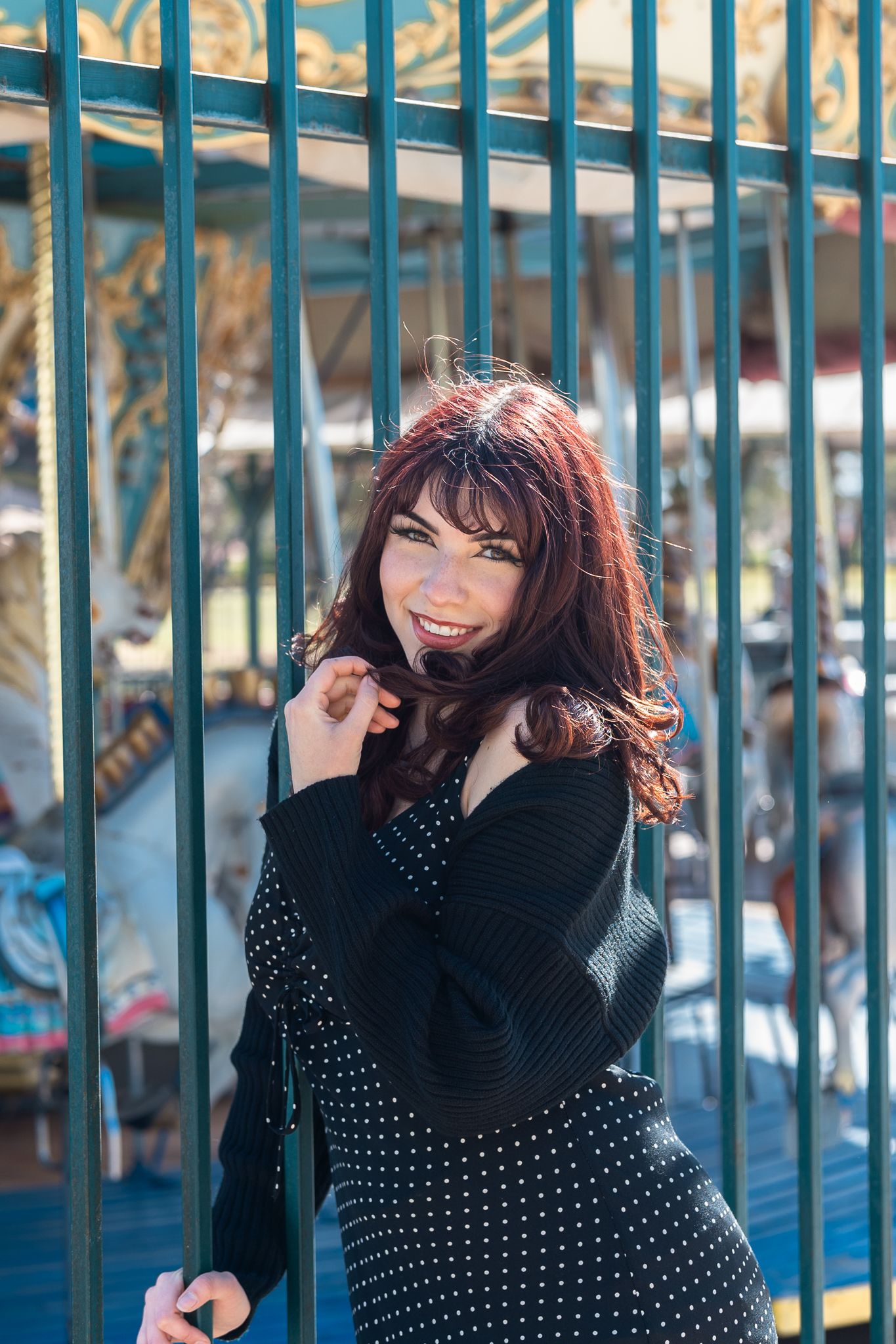 A joyful portrait by decorative blue gates wearing polka dots and a black sweater.