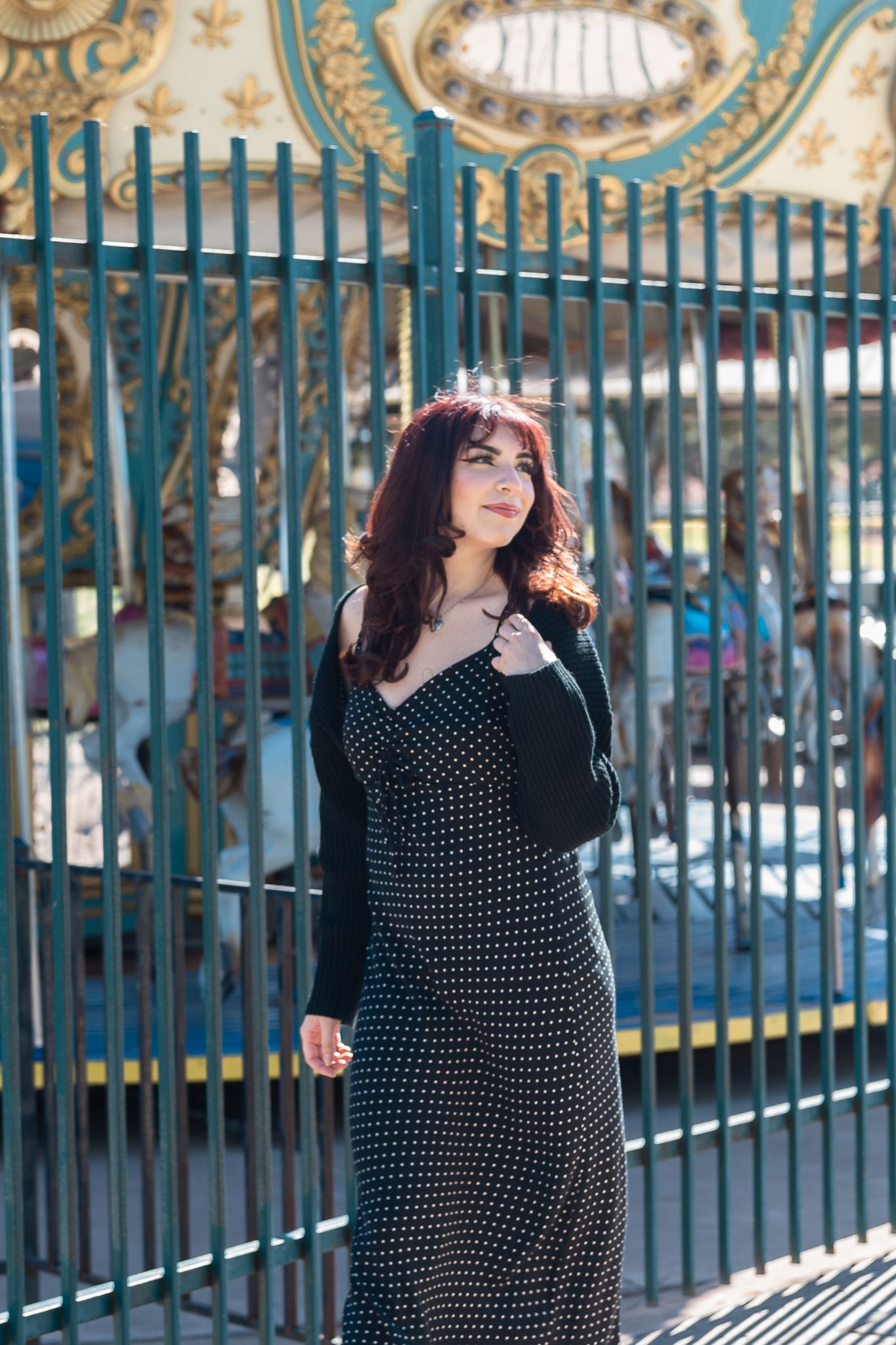 Someone posing in a polka dot dress by ornate blue carousel gates.