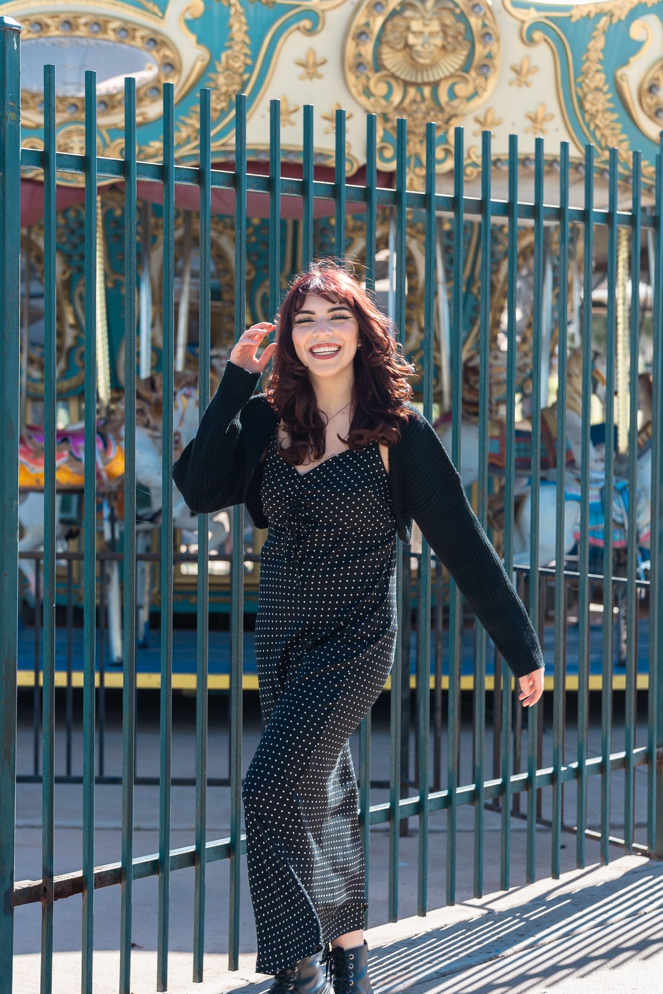 A playful pose against ornate blue gates in a polka dot jumpsuit and cardigan.