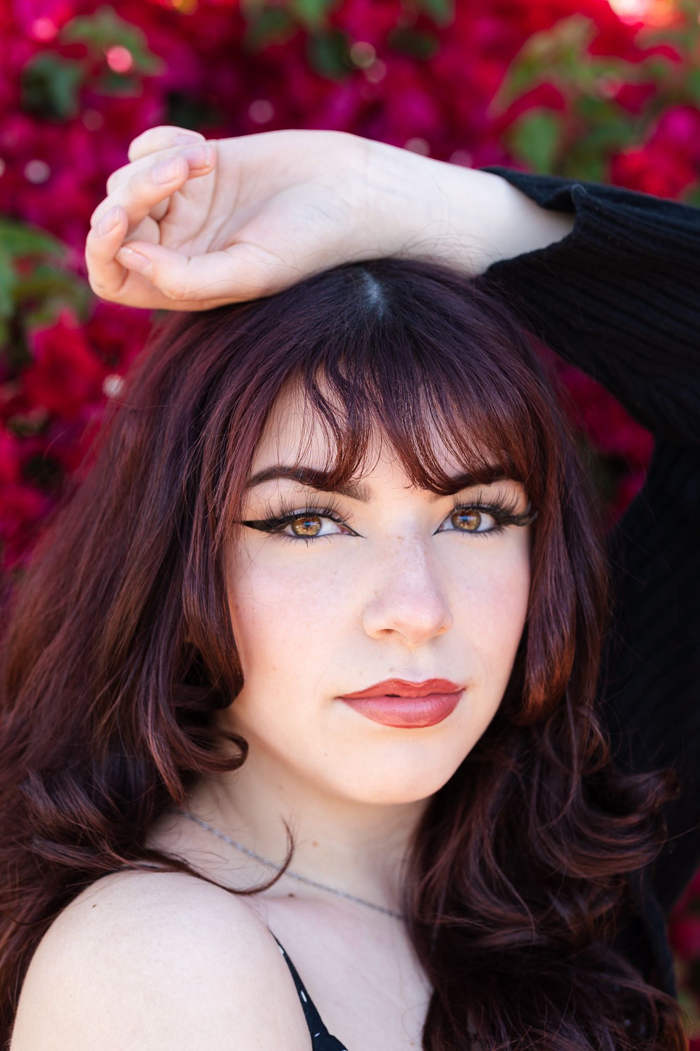 Classic beauty portrait against red flowers with dramatic makeup and styled hair.