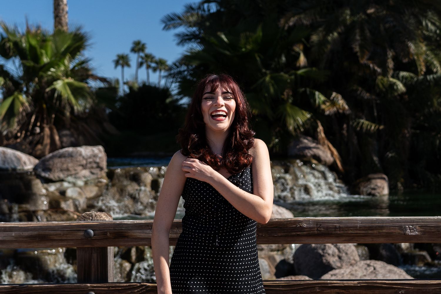 A joyful moment captured in a polka dot dress against a tropical backdrop with palm trees and rocks.