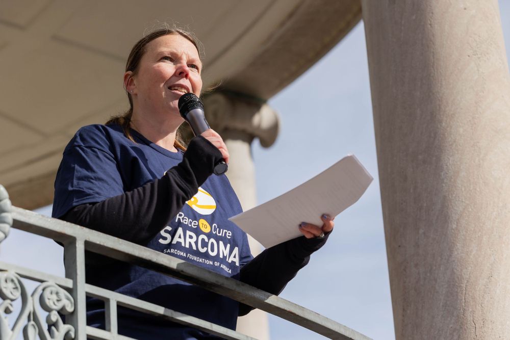 Speaker at podium delivering remarks at outdoor charity race event.