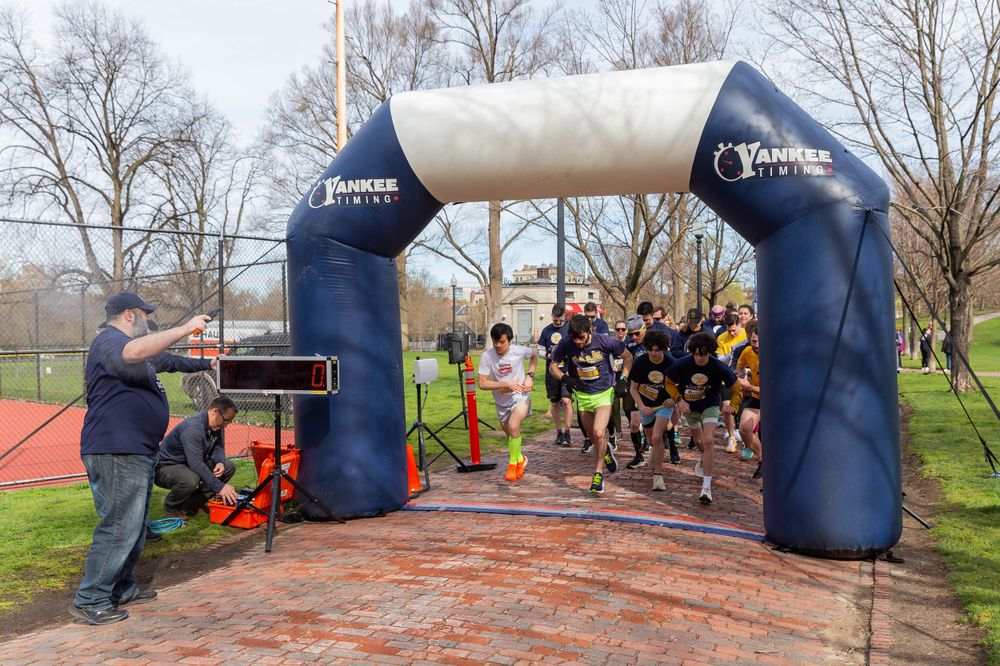 Runners taking off under inflatable blue arch at race start line.