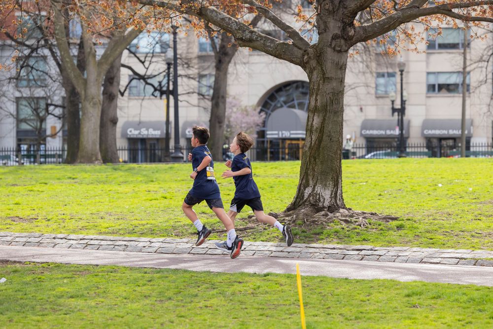 Two runners jogging along tree-lined path during race event.