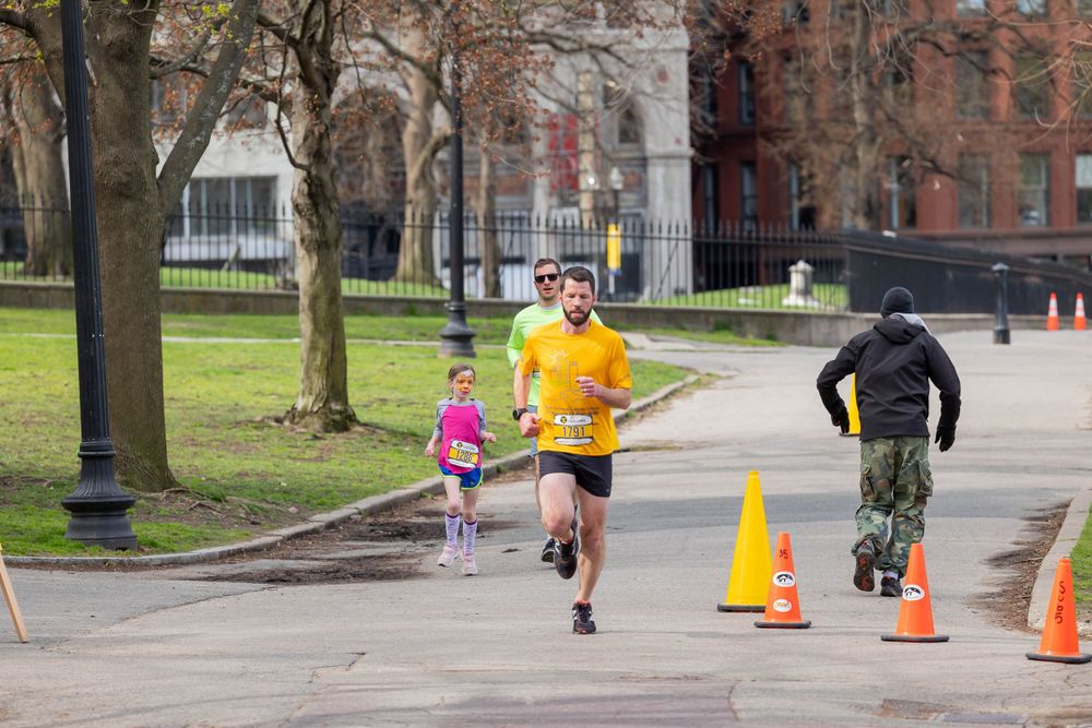 Runners following course marked by orange cones during daytime race.