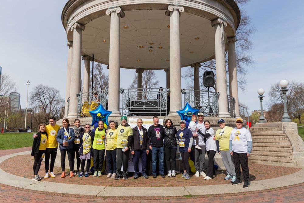 Large group photo of race participants gathered under classical columned structure.