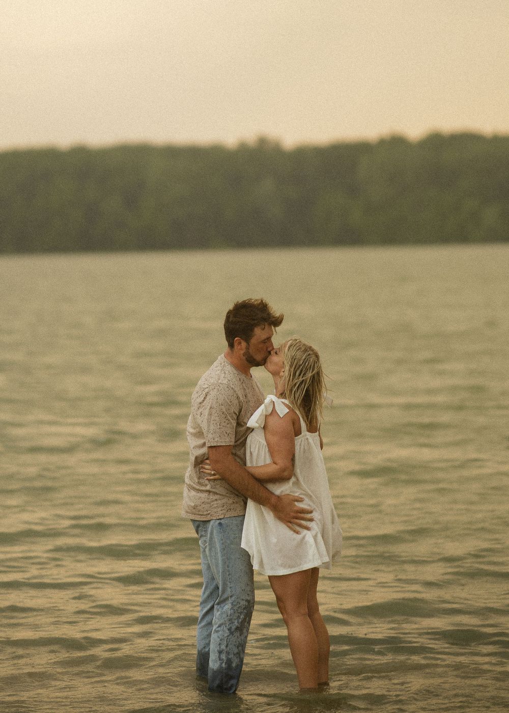 A couple shares a romantic embrace while standing in shallow ocean waters at sunset, creating a dreamy silhouette effect.