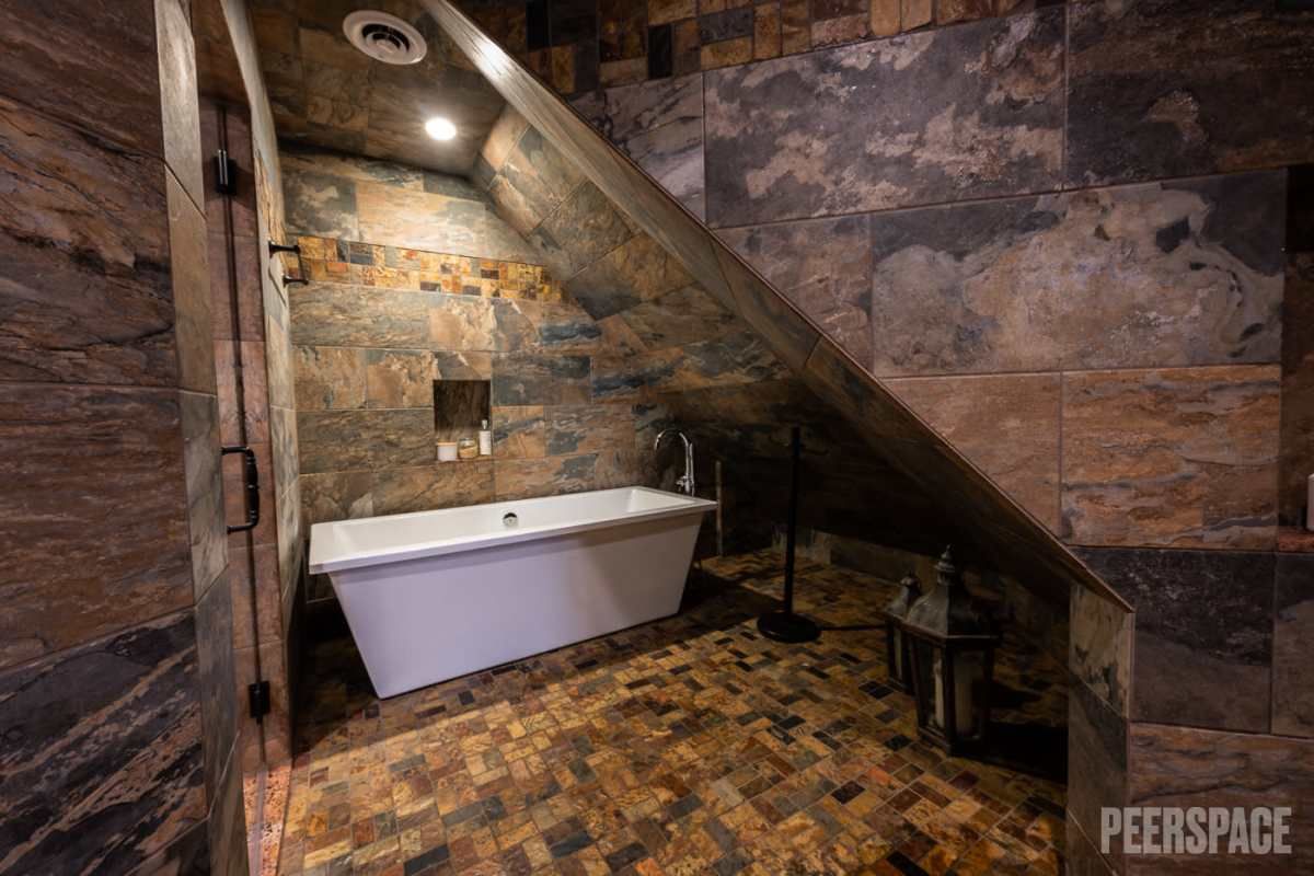 Luxury bathroom featuring freestanding tub and rustic stone walls in an attic-style space.
