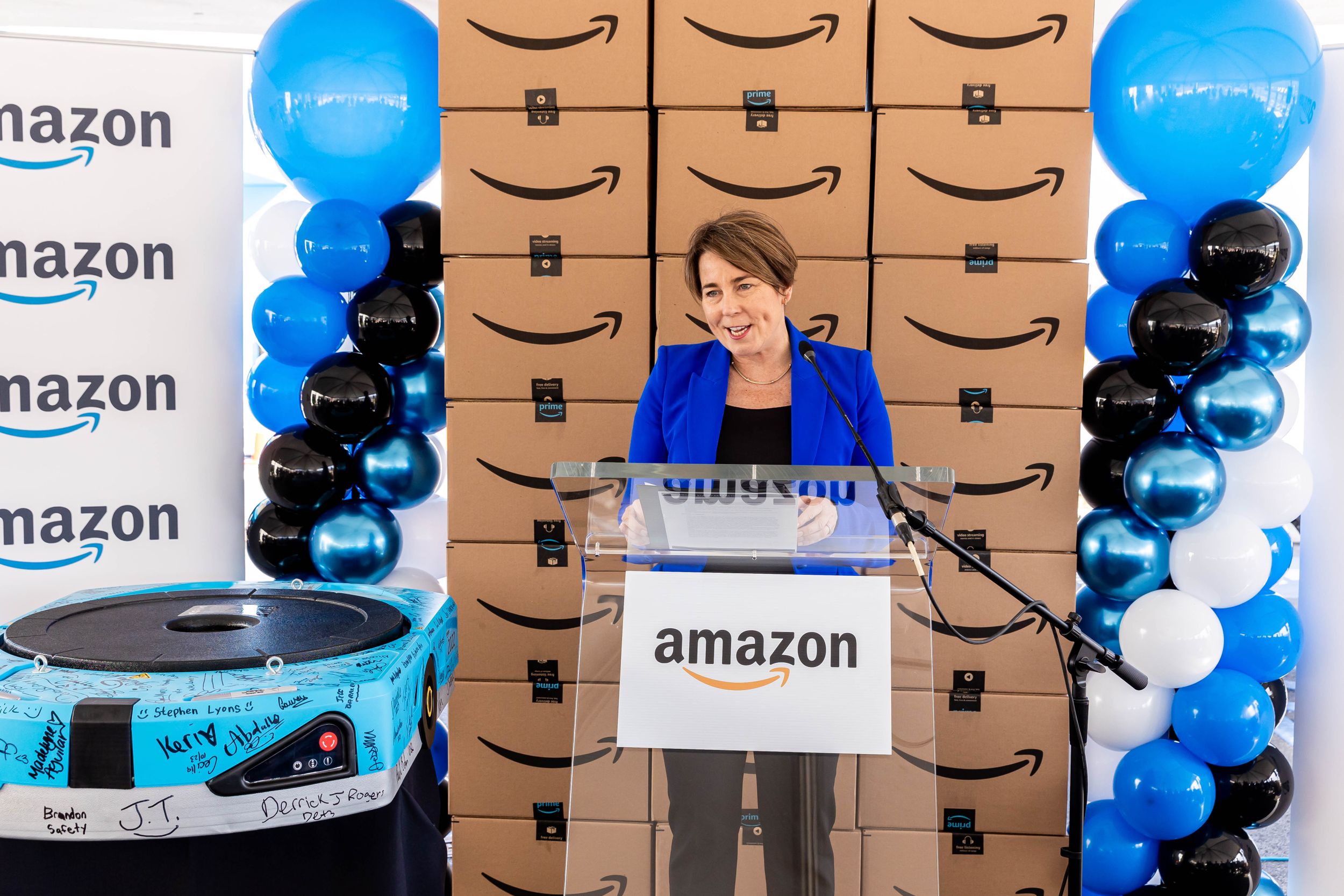 Speaker at Amazon branded podium with blue and black balloon arrangements and company backdrop.