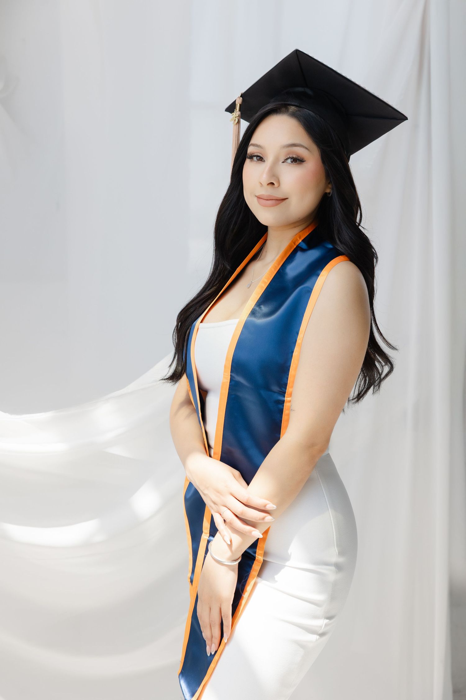 Graduate in cap and gown holds red roses against burgundy background.