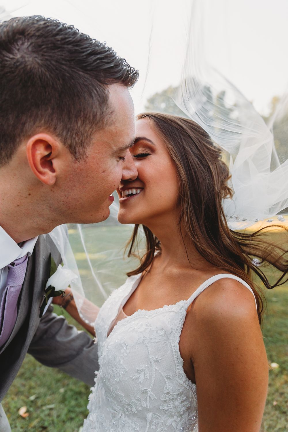 Intimate wedding portrait of a couple sharing a tender moment outdoors with a flowing veil in natural lighting.