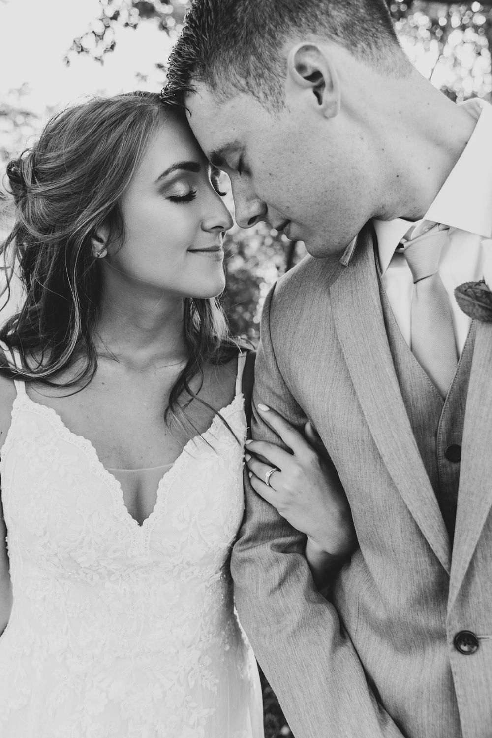 A romantic black and white photo of a couple in wedding attire sharing an intimate moment with their foreheads touching.