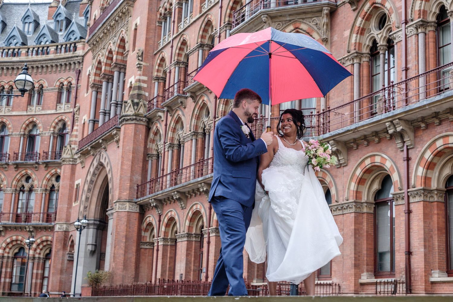 A bride and groom descend a grand marble staircase while holding hands at an elegant wedding venue.