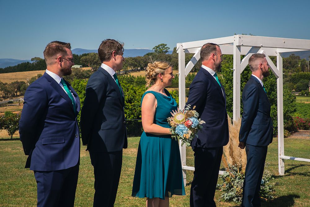 Wedding party members in formal attire stand in line at an outdoor ceremony with mountain views.