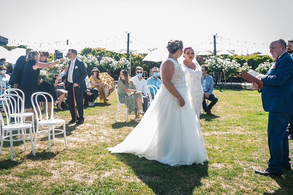 A panoramic view of an outdoor wedding ceremony with white chairs arranged on a grassy field in the summer.