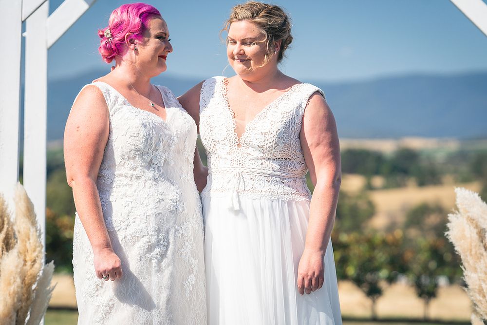 People in white lace dresses gathered outdoors with scenic countryside views in the background.
