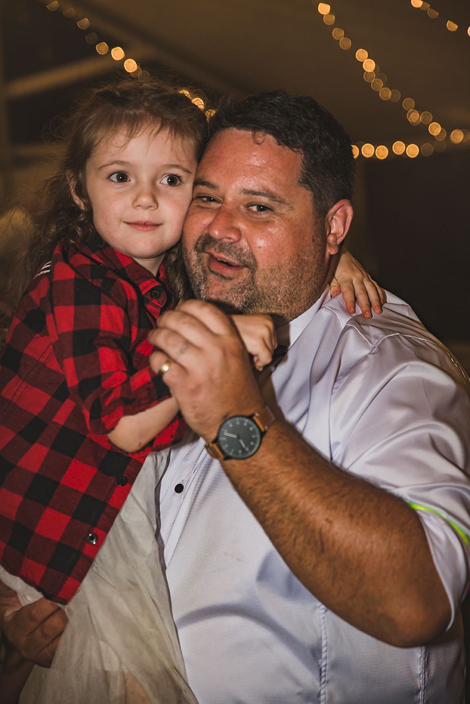 A heartwarming candid moment features a red plaid shirt and white dress shirt during a celebration with twinkle lights.
