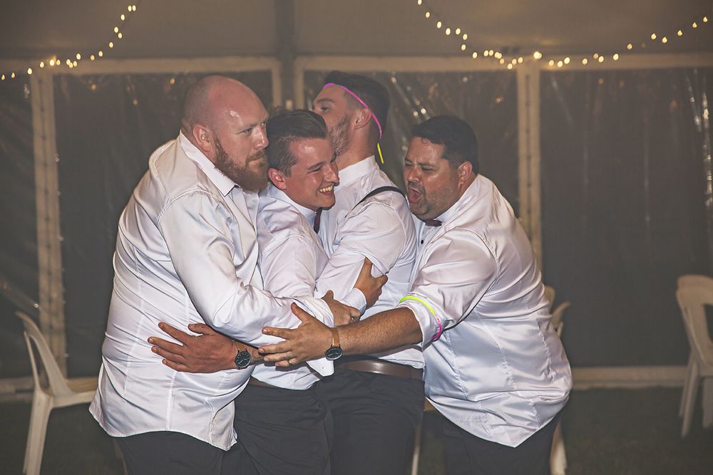A joyful group shares an emotional embrace while wearing matching white shirts at an evening celebration.