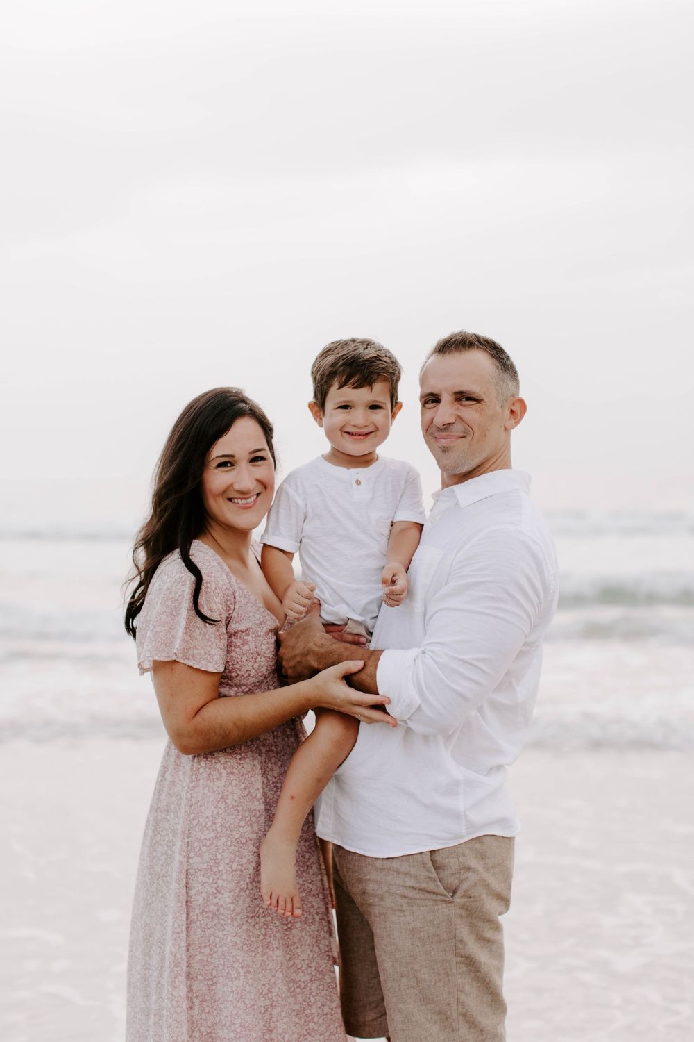 Happy family laughing together during casual beach photo session.