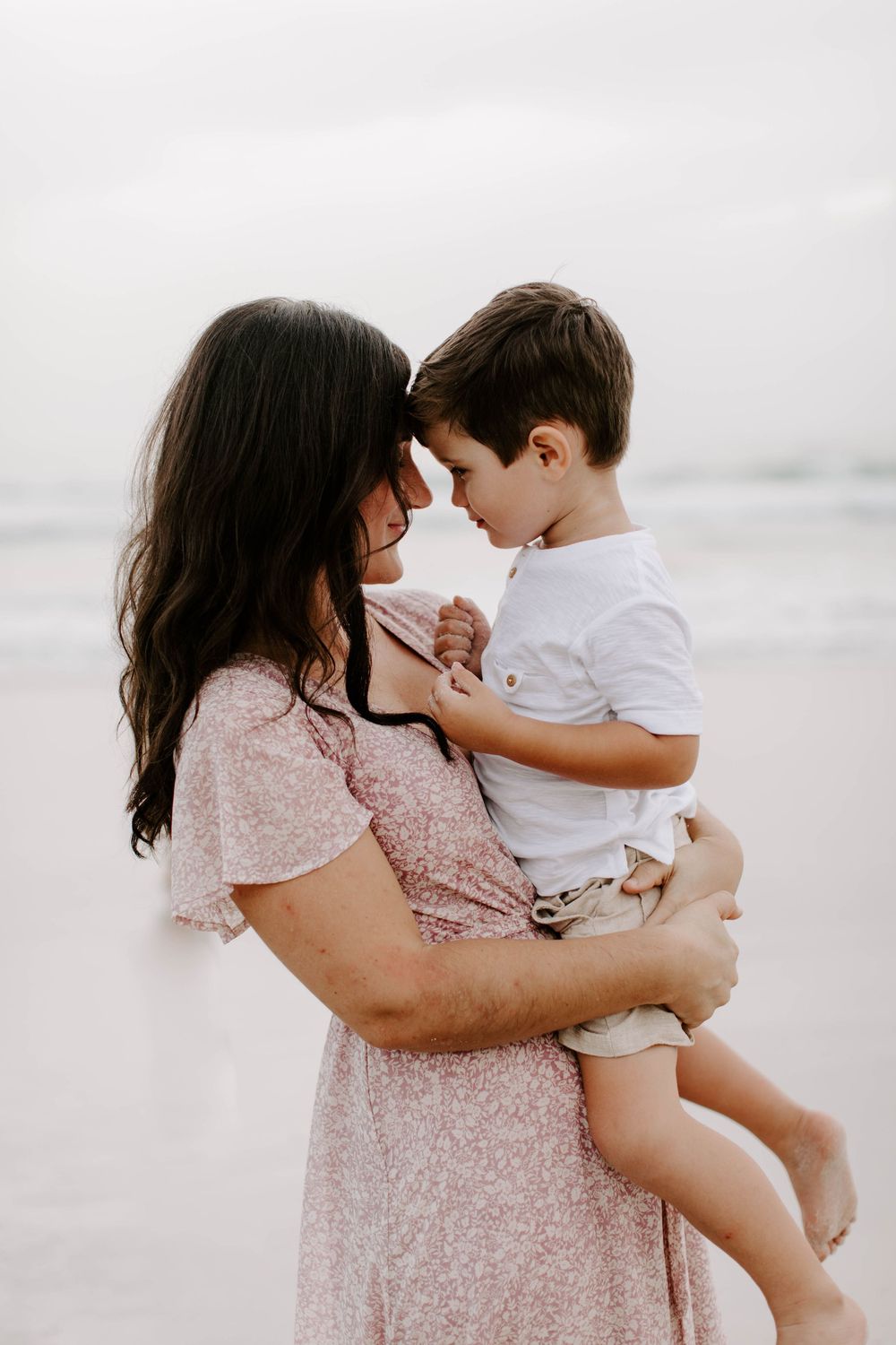 Tender moments between family members captured in soft, muted tones on beach in New Smyrna Beach.