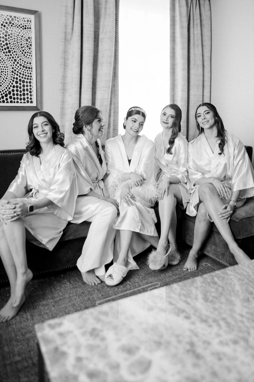 Group of women in matching white silk robes relaxing together on a couch during a casual gathering.