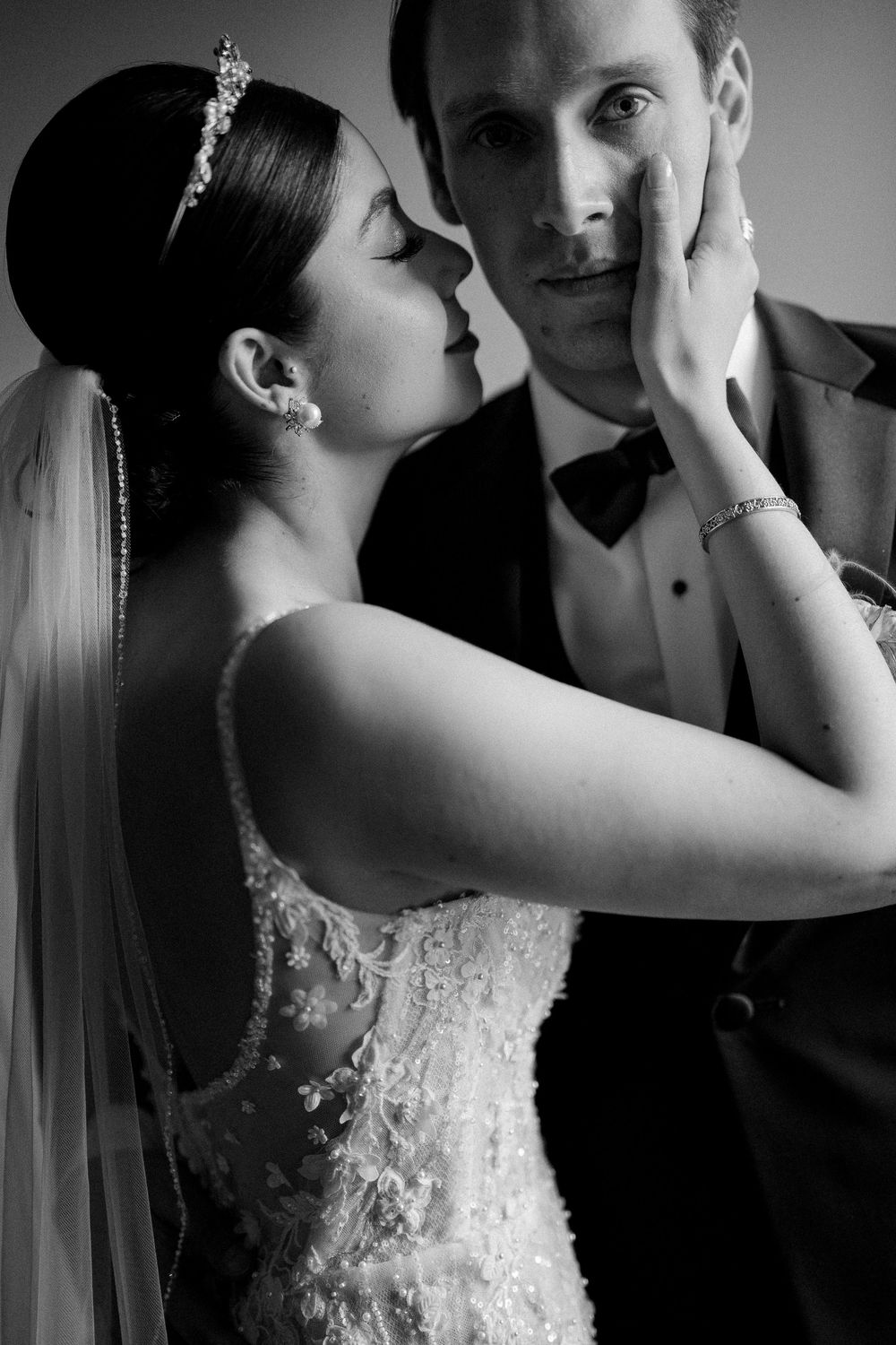 An intimate black and white portrait captures a tender moment between a bride in lace and groom in formal attire.