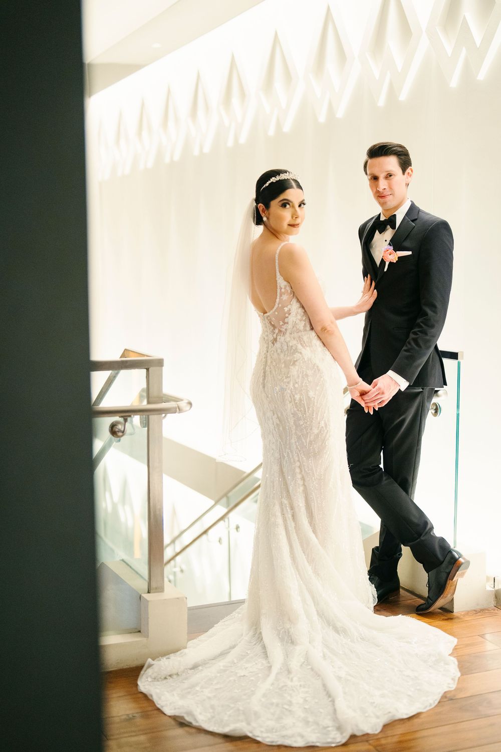 Bride and groom posing together in an elegant stairwell with natural light streaming in through windows.