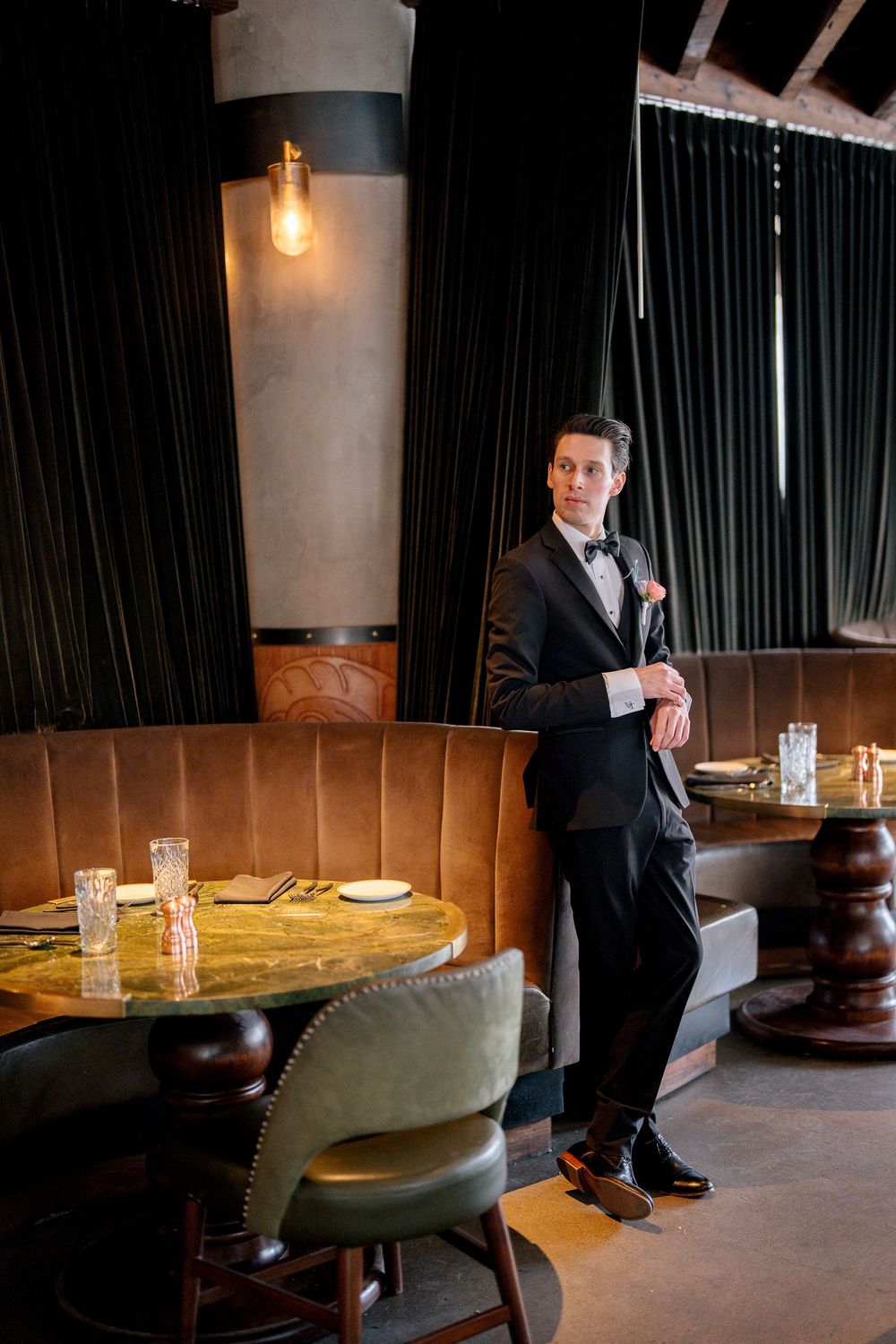A person in a business suit stands in a dimly lit lounge area with wooden accents and vintage-style seating.