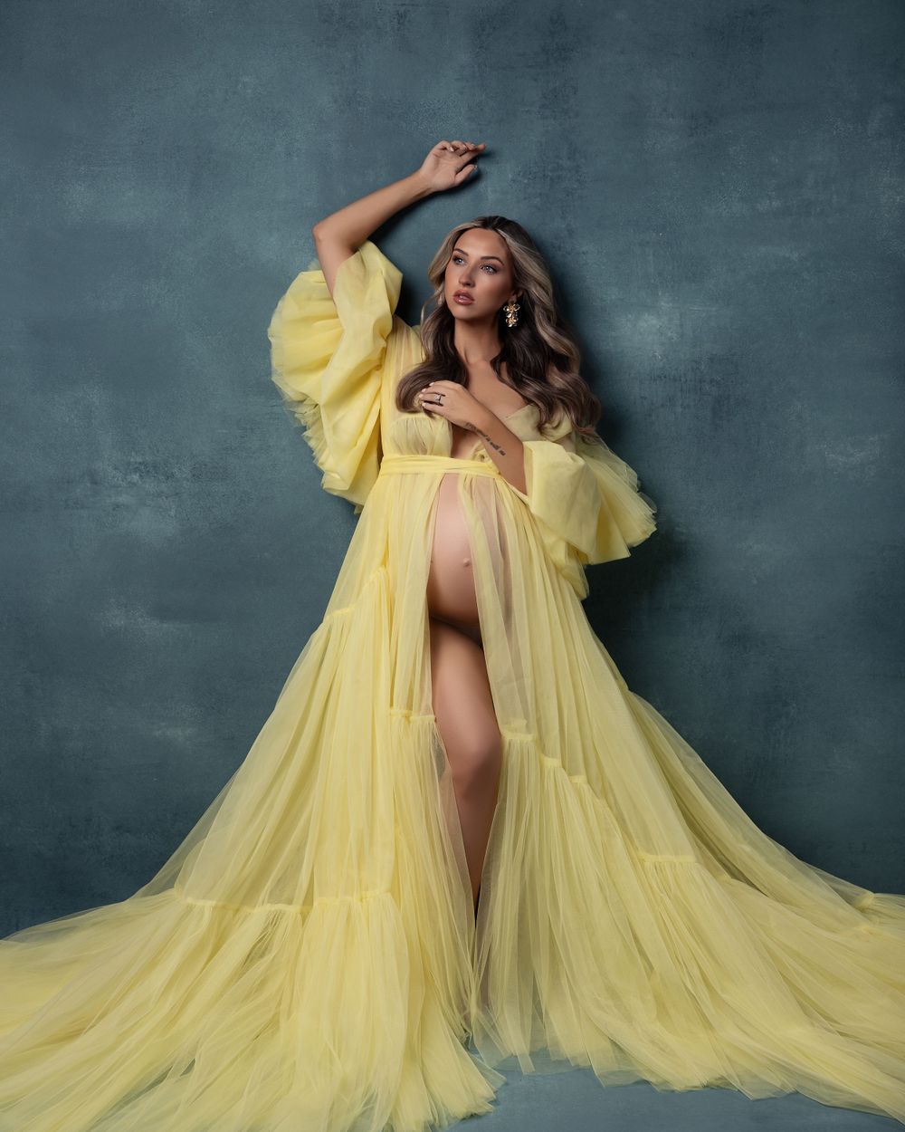 Ethereal fashion portrait featuring a flowing yellow tulle gown against a moody gray backdrop.