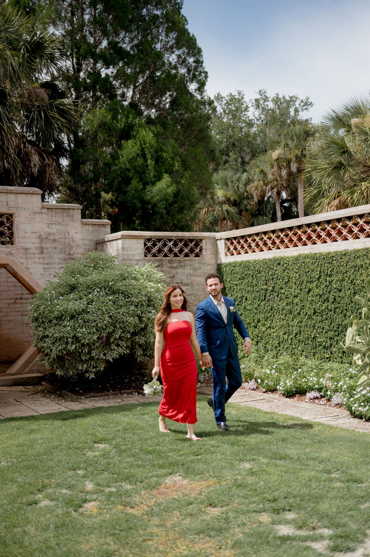 Couple walking together in a sunny backyard garden with green hedges and a lattice wall.