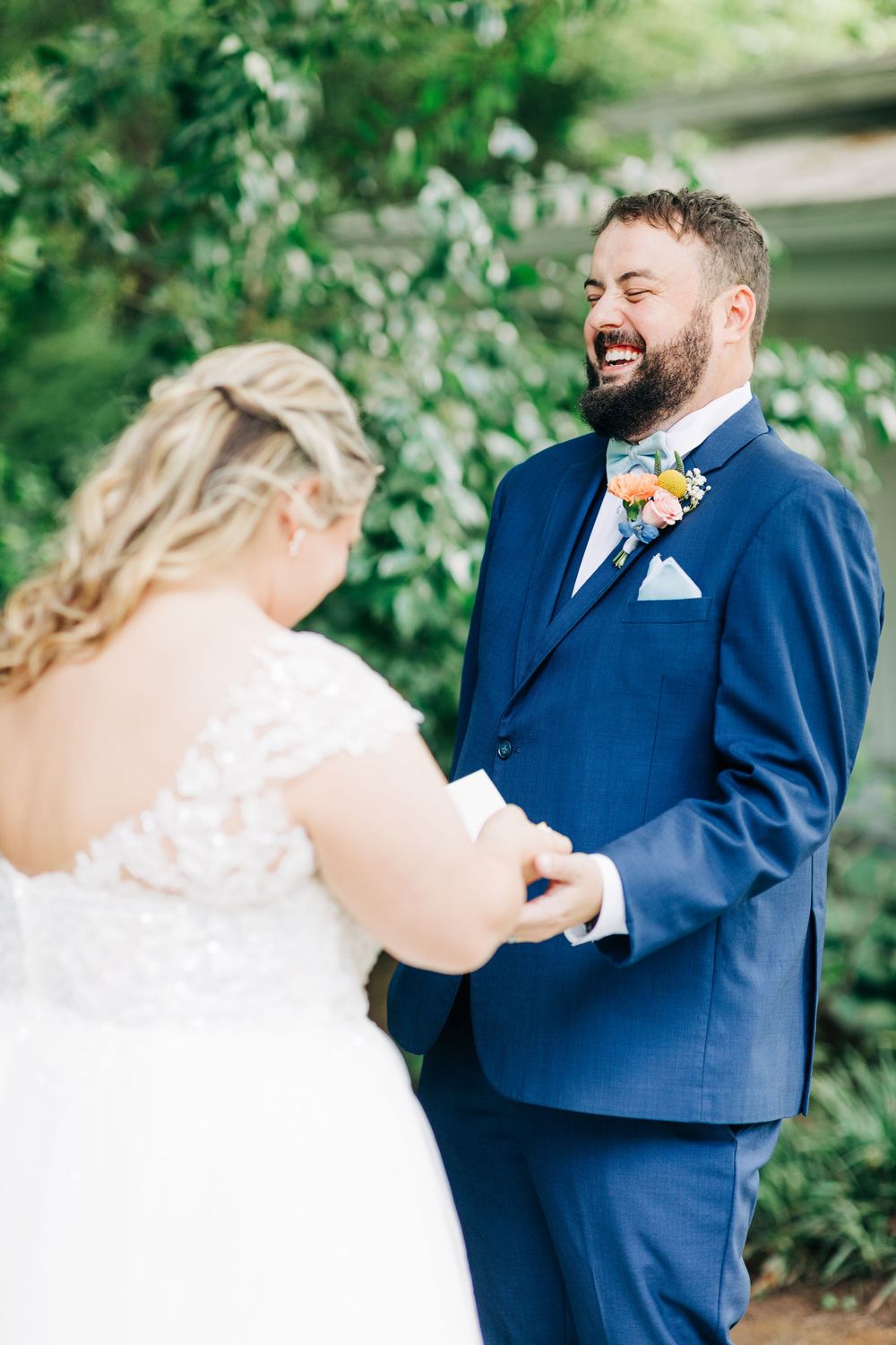 A joyful first look moment between newlyweds during an outdoor garden wedding, with the groom wearing a navy blue suit.